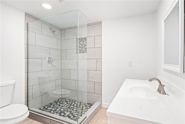 bathroom featuring tiled shower, vanity, hardwood / wood-style flooring, and toilet