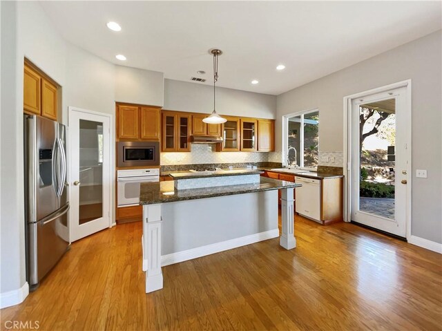 kitchen featuring decorative light fixtures, a center island, stainless steel appliances, and light hardwood / wood-style flooring