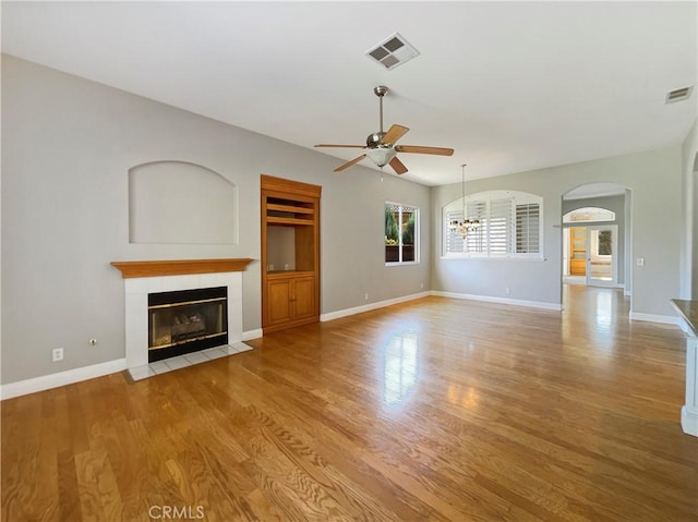 unfurnished living room featuring a tile fireplace, ceiling fan with notable chandelier, and light wood-type flooring