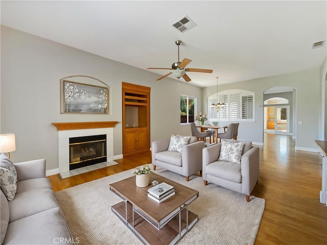 living room featuring ceiling fan, a tile fireplace, and light hardwood / wood-style flooring