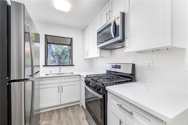 kitchen with white cabinets, appliances with stainless steel finishes, light hardwood / wood-style flooring, and sink