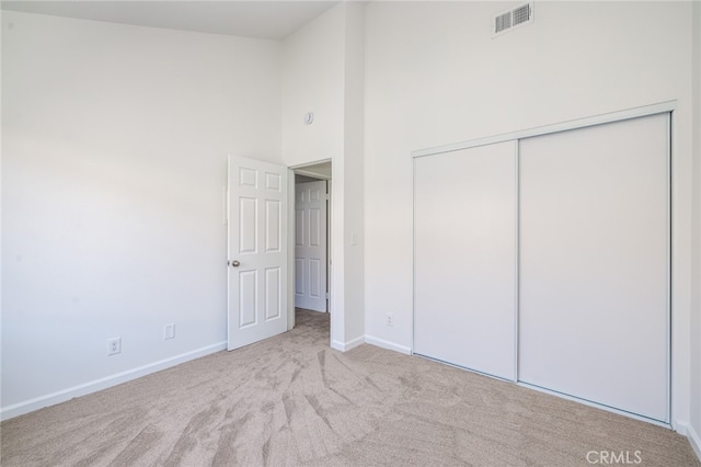 unfurnished bedroom with light carpet, a high ceiling, and a closet