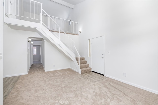 unfurnished living room featuring beam ceiling, light carpet, and a towering ceiling