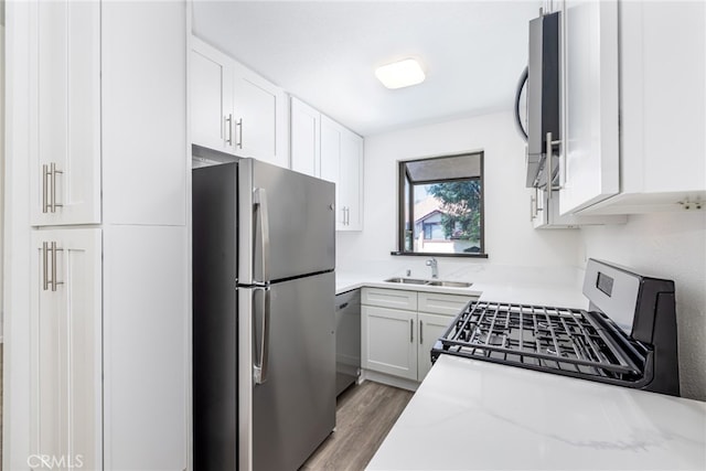 kitchen with light stone countertops, sink, dark wood-type flooring, stainless steel appliances, and white cabinets