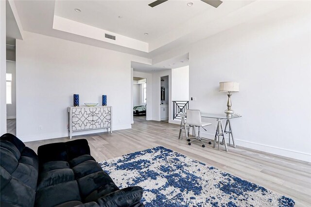 living room with a raised ceiling, ceiling fan, and light hardwood / wood-style floors