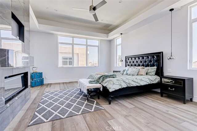 bedroom with a tray ceiling, ceiling fan, a fireplace, and light wood-type flooring