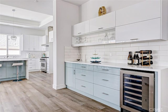 kitchen with light wood-type flooring, beverage cooler, decorative light fixtures, high end stainless steel range, and white cabinetry