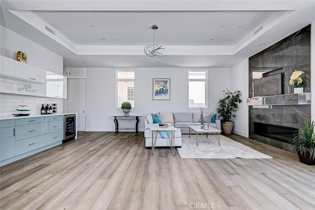 living room with light wood-type flooring, a tray ceiling, beverage cooler, and a large fireplace