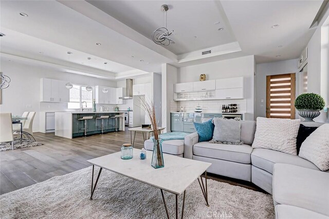 living room featuring an inviting chandelier, sink, light hardwood / wood-style flooring, and a tray ceiling