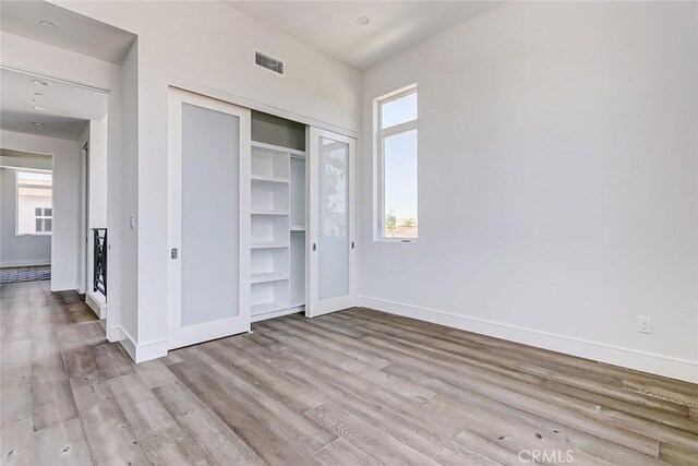 unfurnished bedroom with light wood-type flooring, a closet, and multiple windows