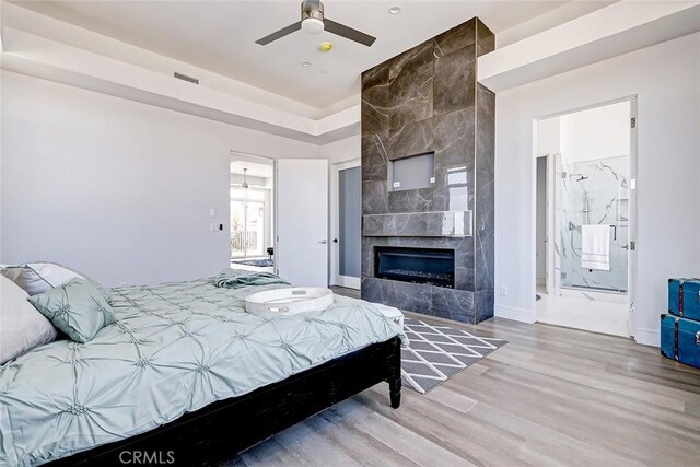 bedroom with light hardwood / wood-style floors, ensuite bath, ceiling fan, and a tiled fireplace