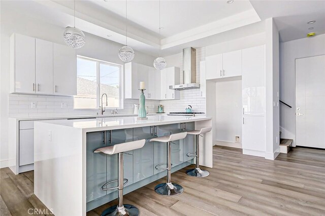 kitchen featuring white cabinetry, a center island, wall chimney exhaust hood, and pendant lighting