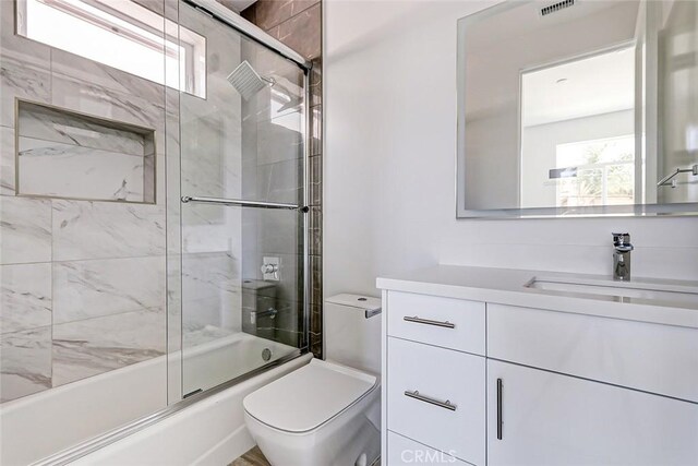 full bathroom with vanity, bath / shower combo with glass door, and toilet