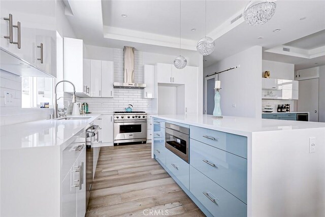 kitchen with wall chimney range hood, appliances with stainless steel finishes, decorative light fixtures, a kitchen island, and white cabinetry