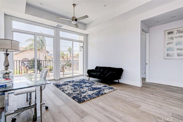 sitting room with a raised ceiling, light hardwood / wood-style flooring, and ceiling fan