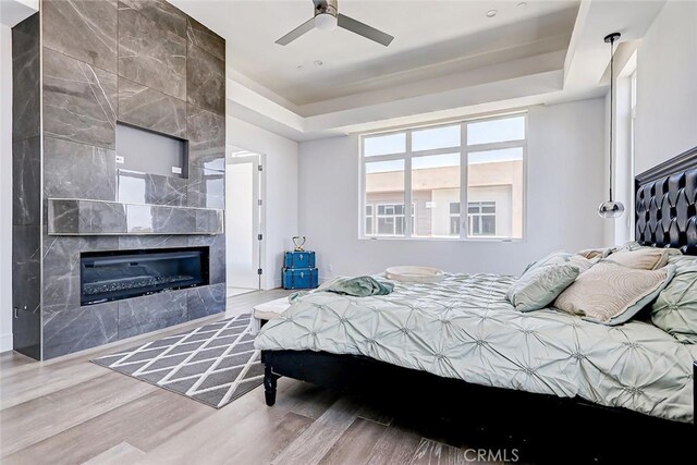 bedroom featuring a raised ceiling, a tile fireplace, ceiling fan, and hardwood / wood-style floors