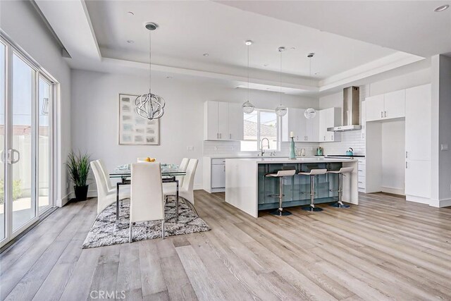 dining space with a tray ceiling, an inviting chandelier, light hardwood / wood-style floors, and sink