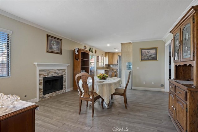 dining space featuring light wood-type flooring, a fireplace, a wealth of natural light, and ornamental molding