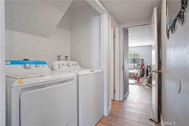 laundry area featuring light wood-type flooring, a textured ceiling, and washing machine and clothes dryer