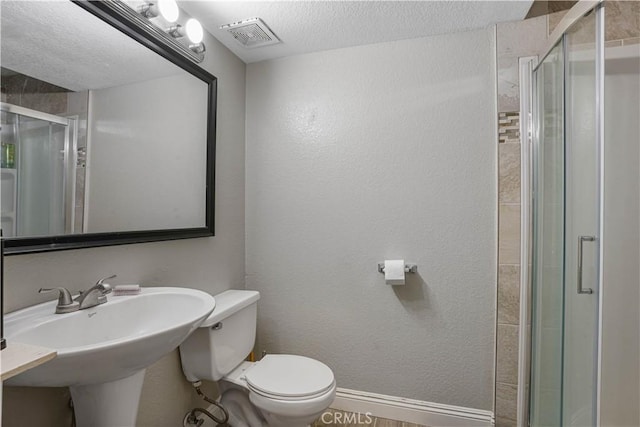 bathroom featuring a textured ceiling, toilet, a shower with shower door, and sink