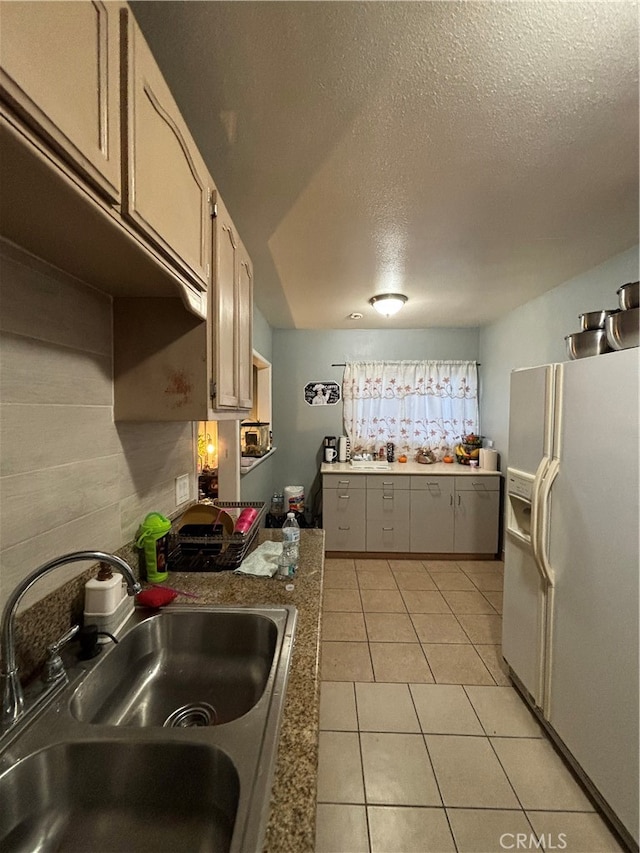 kitchen featuring light tile patterned floors, white fridge with ice dispenser, a textured ceiling, and sink