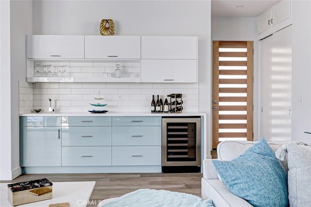 bar featuring decorative backsplash, white cabinets, beverage cooler, and light wood-type flooring