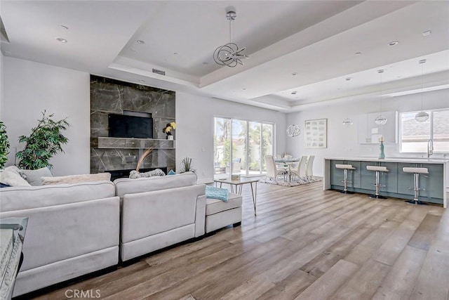 living room with a raised ceiling, a premium fireplace, sink, and light hardwood / wood-style flooring