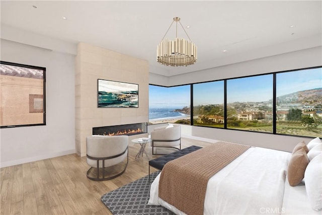 bedroom featuring light hardwood / wood-style floors, a water view, a fireplace, and an inviting chandelier