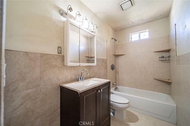 full bathroom with vanity, tile patterned flooring, tiled shower / bath combo, toilet, and tile walls