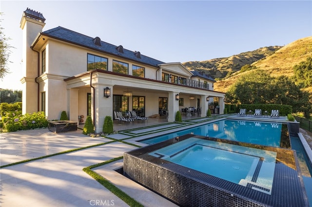 back of property featuring a balcony, a swimming pool with hot tub, a mountain view, and a patio