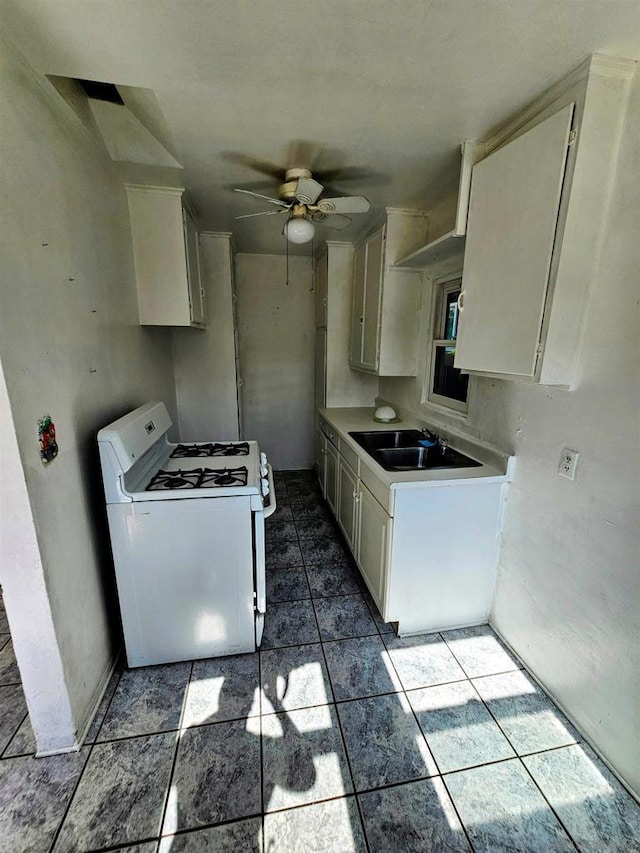 kitchen with white gas stove, ceiling fan, white cabinetry, and sink