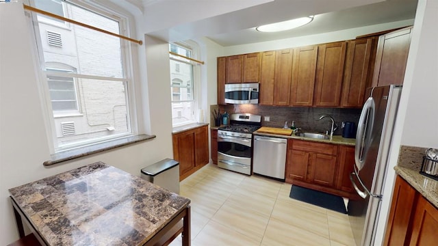 kitchen with light stone countertops, appliances with stainless steel finishes, backsplash, sink, and light tile patterned floors