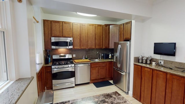 kitchen with sink, light stone countertops, light tile patterned floors, tasteful backsplash, and stainless steel appliances