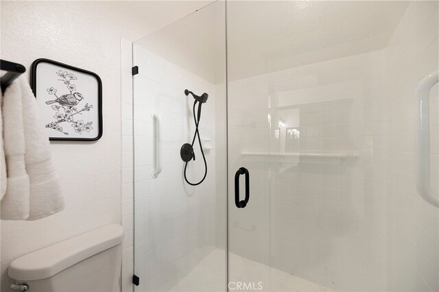 bathroom with a shower with shower door and toilet