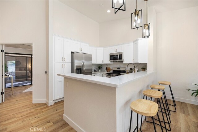 kitchen with white cabinets, kitchen peninsula, a kitchen bar, light hardwood / wood-style flooring, and stainless steel appliances