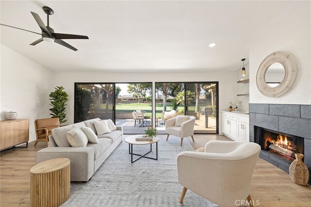 living room featuring a tile fireplace, light hardwood / wood-style floors, and ceiling fan