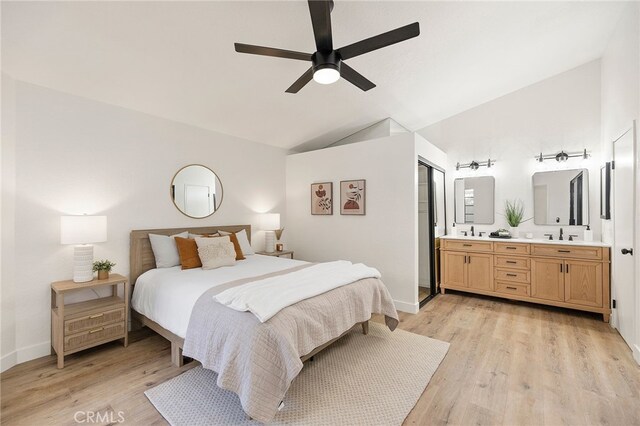 bedroom featuring light hardwood / wood-style floors, vaulted ceiling, ceiling fan, ensuite bath, and sink