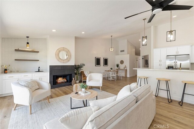 living room featuring ceiling fan with notable chandelier, a tiled fireplace, light hardwood / wood-style floors, and high vaulted ceiling