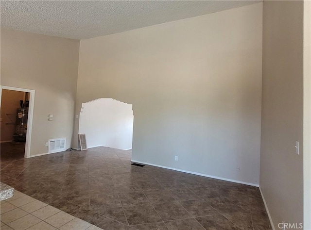 empty room with a textured ceiling, strapped water heater, and dark tile patterned floors