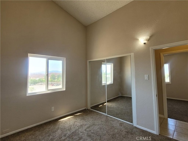 unfurnished bedroom with dark carpet, lofted ceiling, a textured ceiling, and a closet