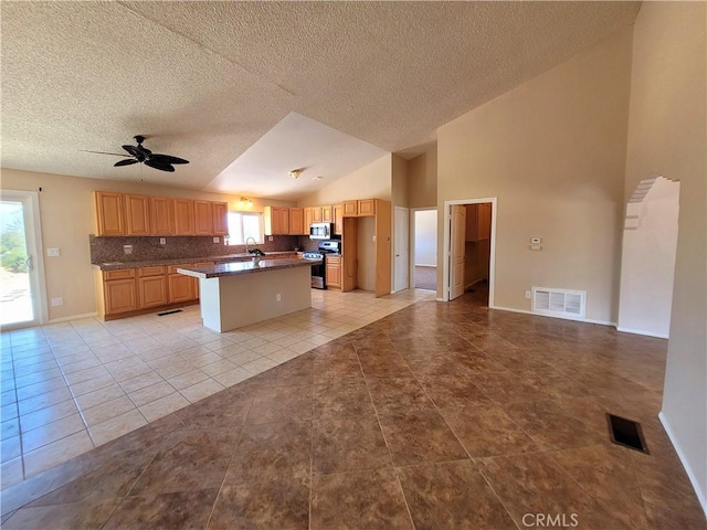 kitchen with ceiling fan, tasteful backsplash, lofted ceiling, a kitchen island, and appliances with stainless steel finishes