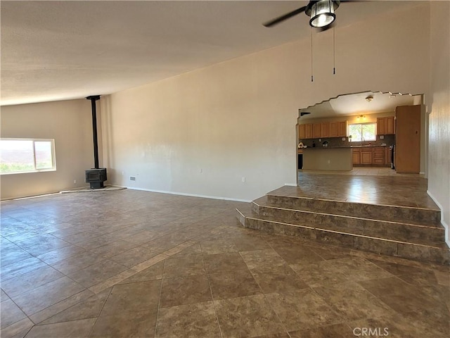 unfurnished living room featuring a wood stove, ceiling fan, and lofted ceiling