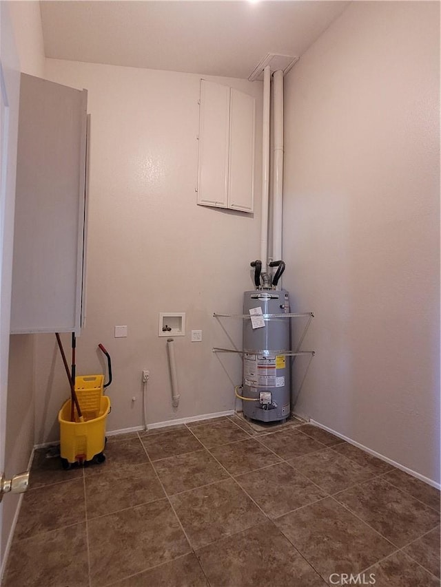 clothes washing area featuring water heater, hookup for a washing machine, and dark tile patterned floors