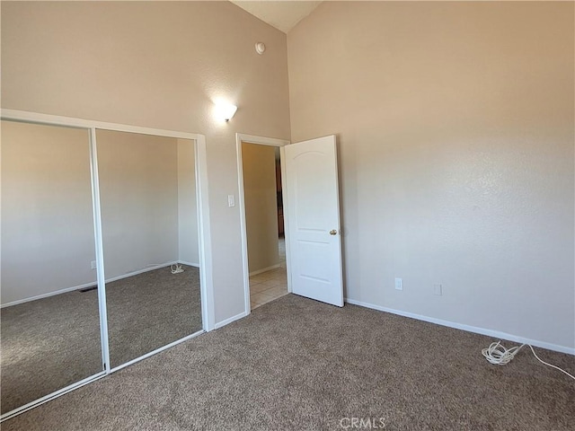 unfurnished bedroom featuring dark colored carpet, high vaulted ceiling, and a closet