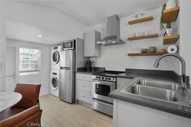 kitchen featuring sink, wall chimney exhaust hood, appliances with stainless steel finishes, light wood-type flooring, and stacked washer and dryer