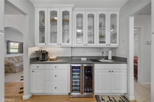 bar with light hardwood / wood-style floors, white cabinetry, beverage cooler, and sink