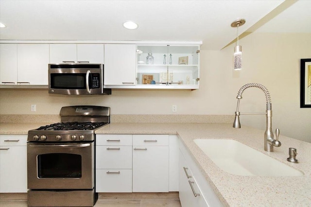 kitchen featuring white cabinetry, sink, light stone countertops, hanging light fixtures, and stainless steel appliances