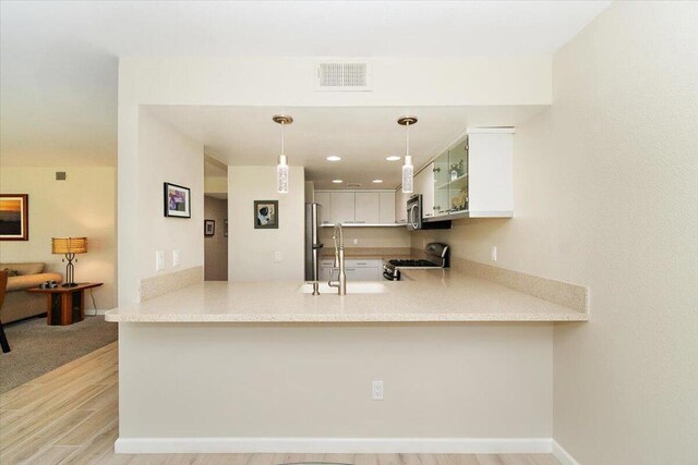 kitchen with kitchen peninsula, stainless steel appliances, decorative light fixtures, light hardwood / wood-style flooring, and white cabinets