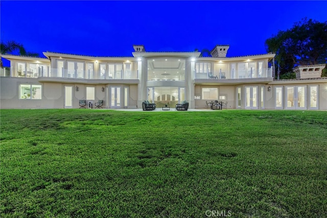 back house at twilight featuring a lawn and a patio area