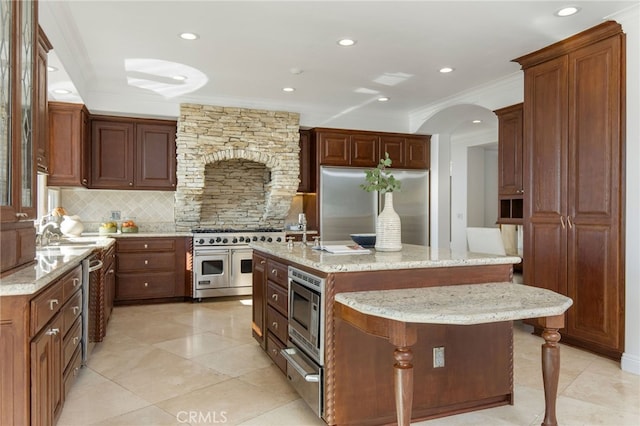 kitchen featuring light stone counters, a kitchen island with sink, appliances with stainless steel finishes, a breakfast bar, and decorative backsplash